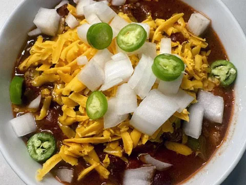 A bowl of chili topped with cheddar, onion and jalapeño